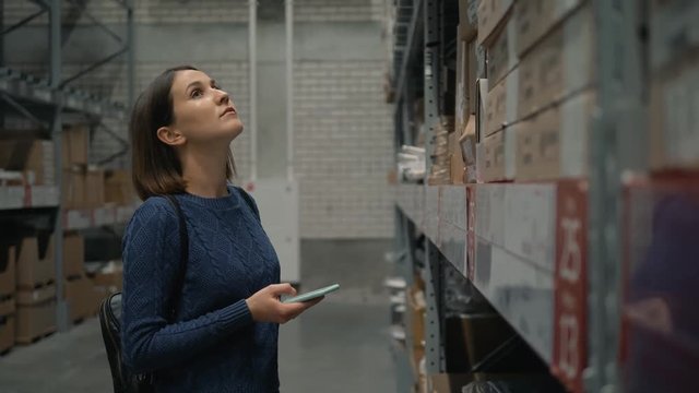Woman with a phone looking for a product in a warehouse store