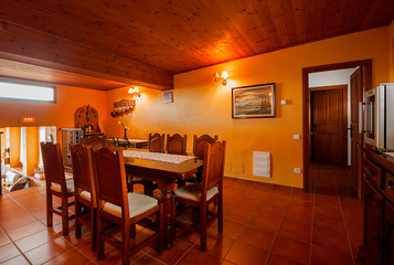 Nice warm interior of dining room with large wooden table and chairs in a rustic style. Country house or hotel. Wooden beams and walls.