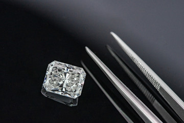 Radiant cut diamond with tweezers on black reflection background