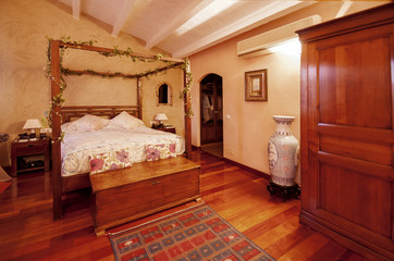 Fototapeta premium Nice warm interior of bedroom in a rustic style in country house or hotel. Wooden beams and walls made of natural stone. Mediterranean style home.