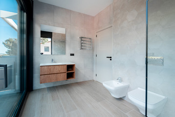 Modern bathroom with a glass bathtub and luxury washbasin. The walls and floor are covered with modern tiles.