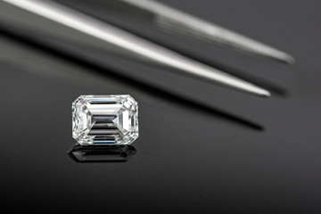 Emerald cut diamond with tweezers on black reflection back ground