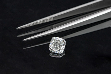 Cushion cut diamond with tweezers on black reflection background