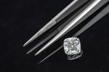 Cushion cut diamond with tweezers on black reflection background