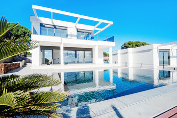 Luxury modern white house with large windows overlooking a Mediterian landscaped garden with palm trees and  blue swimming pool. High tech style villa. Vacation home or hotel. Modern loft design.ees a