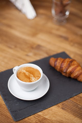 Breakfast with espresso cup of hot coffee and croissant on a black stone plate