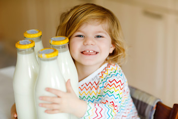 Adorable toddler girl drinking cow milk for breakfast. Cute baby daughter with lots of bottles. Healthy child having milk as health calcium source. Kid at home or nursery in the morning.