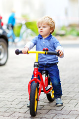 Active blond kid boy in colorful clothes driving balance and learner's bike or bicycle in domestic...