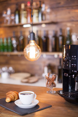 Modern coffee machine next to a cup of esoresso coffee on wooden counter bar.