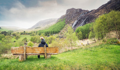 Obraz premium A girl sitting on the wooden bench and looking at the waterfall in Kenmare