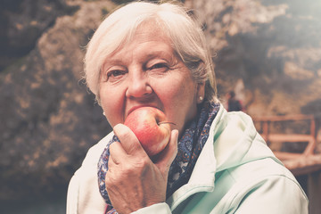 Healthy looking senior woman with grey hair eating apple outside in the park