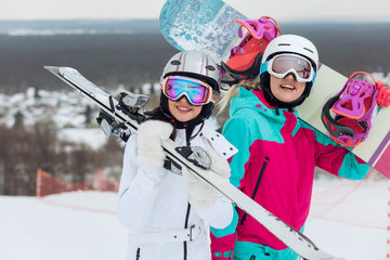 happy two girls holding equipment for snowvoarding and skiing and looking at the camera , women...