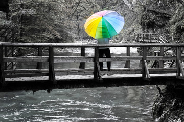 Mature woman standing on a wooden bridge over river with colorful umbrella on a sunny autumn day black and white