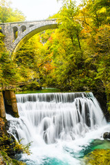 Autumn forest colors with turquoise waterfall and old rocky train bridge in natural park of Vintgar river gorge Slovenia