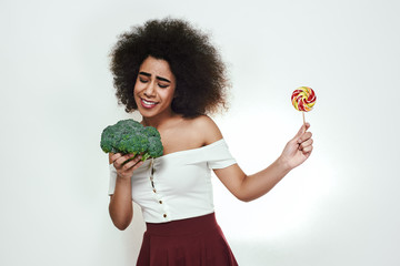 I choose healthy food! Pretty afro american woman is facing a choice of healthy broccoli or...