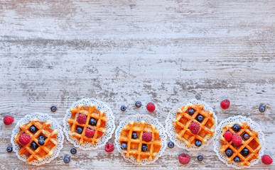 Traditional waffles with fresh  raspberries and blueberries on lace doily on wooden background.  Top view, copy space, flat lay . - obrazy, fototapety, plakaty