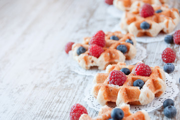 Traditional waffles with fresh  raspberries and blueberries on lace doily on wooden background.