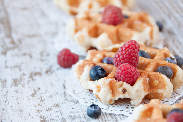 Traditional waffles with fresh  raspberries and blueberries on lace doily on wooden background.