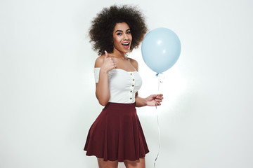 It was the best birthday party! Portrait of cheerful and happy afro American woman showing thumb up, holding blue balloon and smiling at camera