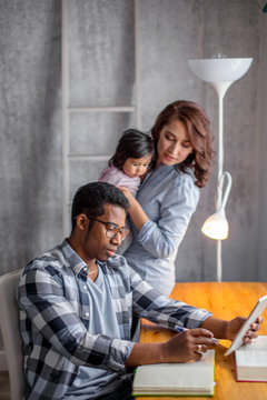 young pleasant man rewritng information from the laptop, close up photo. woman with a baby on the background of the photo. man solving family's problems