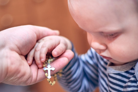 A Child Takes A Rosary From His Dad's Hand