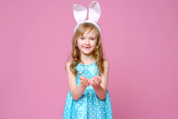 Obraz na płótnie Canvas Cute little blonde girl in the shape of an Easter Bunny and a blue dress with a pea pattern holds her fingers . Concept of the celebration, advertising and fashion. happy Easter. Selective focus.