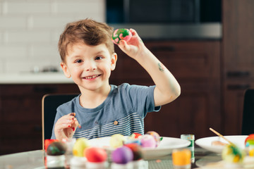 Happy little caucasian boy of 4-5 years feeling interest and joy, painting the easter eggs at...