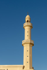 Fototapeta na wymiar A spire and minaret of a white and orange mosque with a blue sky background.