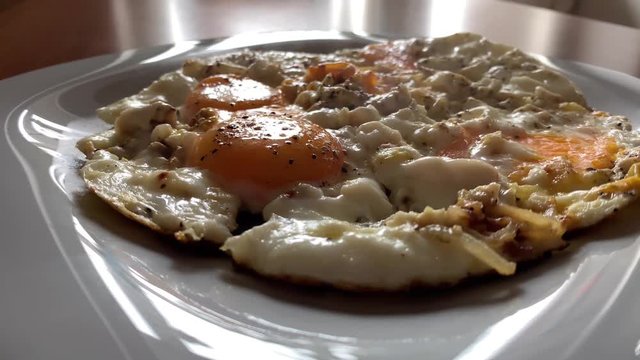 Video of cooking of fried eggs from several eggs with onions and black pepper, liquid egg white, a teflon frying pan, bubbles, steam, omelet