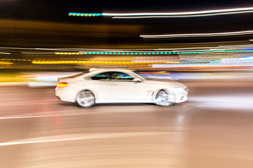 Fototapeta na wymiar Car rolling at full speed through the city at night, image of panning, with defocused background lights.