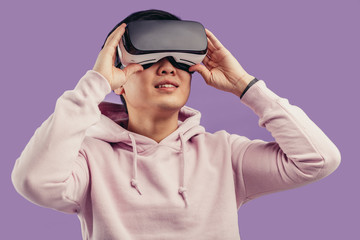 Korean young man surprised by something in virtual reality, wearing virtual reality glasses showing...