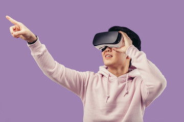 Amazed positive chinese male gamer wearing virtual reality goggles headset, vr box, posing isolated in studio over violet background. Connection, technology, new generation, progress concept.