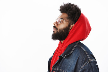 Profile shot of cool and stylish confident and self-satisfied african american male rap-singer wearing hoodie and denim jacket looking with raised chin left being self-assured over gray background