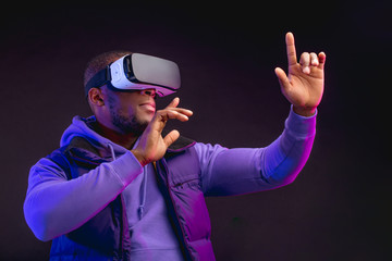 Young dark-skinned man dressed in outdoor wear having on head mobile virtual reality headset for playing 3D game but Mankind meets a new era of controlling real world objects from virtual reality.