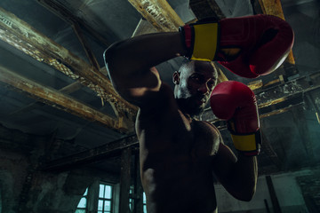Hands of boxer over dark gym background. Strength, attack and motion concept. Fit african american model in movement. Naked muscular athlete in red gloves. Sporty man during boxing.