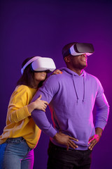 Young interracial couple having first experience of using virtual reality headset, standing joyful...