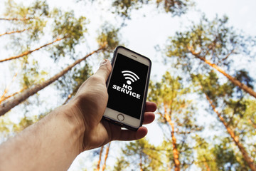 Male hand is holding a phone with sign no service  above his head against the background of trees...