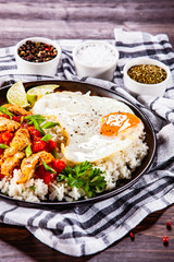 Grilled chicken meat with rice and fried egg on wooden table