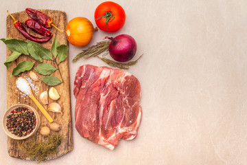 Raw pork shoulder. Spices, dry herbs, onions, garlic, rosemary, bay leaf, hot pepper, nutmeg, pepper mix, tomatoes. Ingredients for marinating meat. Wooden vintage board, stone background, top view.