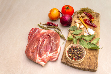 Raw pork shoulder. Spices, dry herbs, onions, garlic, rosemary, bay leaf, hot pepper, nutmeg, pepper mix, tomatoes. Ingredients for marinating meat. Wooden vintage board, stone background, close up.