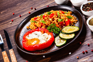 Fried egg, groats and vegetables on wooden table