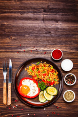 Fried egg, groats and vegetables on wooden table