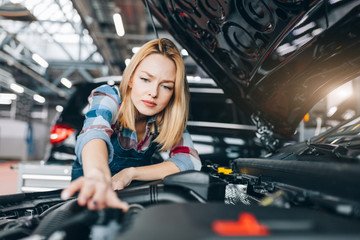 young female worker stretching her arm to the engine compartmant, device . close up photo. the difficulties of fixing a car