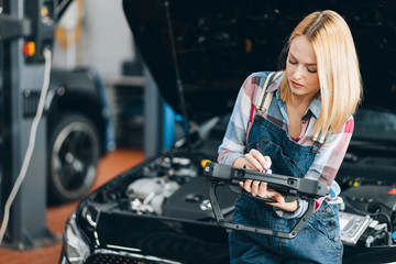 good looking blond girl checking a car by using a tablet, close up photo.diagnostic of new vehicle