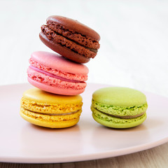 Colorful macarons on pink plate on a white wooden surface, side view. Close-up.