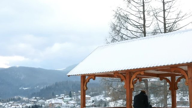 Amazing winter landscape. Man standing in wooden arbor over fascinating hills and countryside covered with snow.