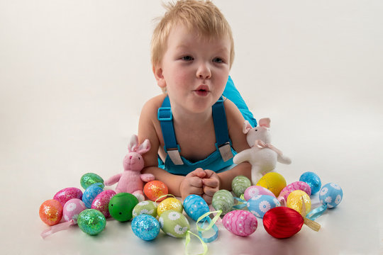 Little blond kid boy coloring eggs for Easter holiday in domestic room, indoors. Child holding basket with painted eggs. Child having fun and celebrating feast with easter toy bynny