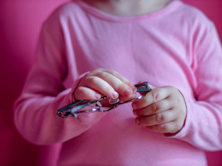 Portrait of funny child in a pink T-shirt in new glasses is playing with computer tablet on pink background. boy is proud of his glasses, clothes and shoots