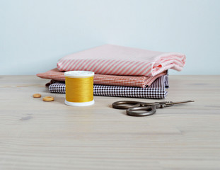 Mustard thread spool , cotton fabrics, wooden buttons and retro scissors on the table
