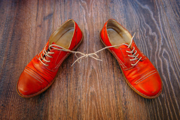 April Fool?s Day Shoes. Casual  womans shoelaces tied together at home in the living room. Red shoes with wooden background